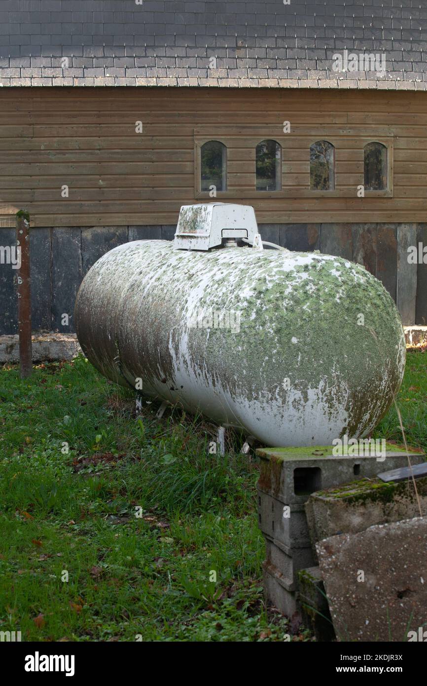 Un réservoir de gaz est placé dans un jardin, il est recouvert de mousse de lichen, il est entouré de matériaux de construction. Banque D'Images