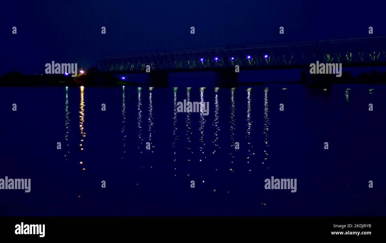 nuit, dans l'eau, le pont et ses lumières sont réfléchis. Un long pont sur la rivière. Photo de haute qualité Banque D'Images