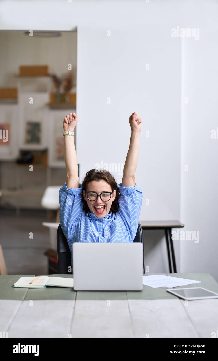 Jeune femme heureuse élève les mains gagnant en ligne regardant l'ordinateur portable. Banque D'Images