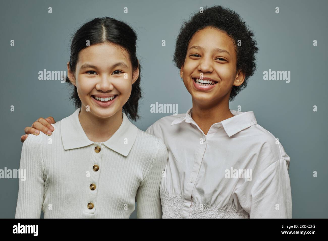 Deux filles chaleureuses et chaleureuses en chemises blanches rient et regardent la caméra tout en posant pendant la séance photo en studio Banque D'Images