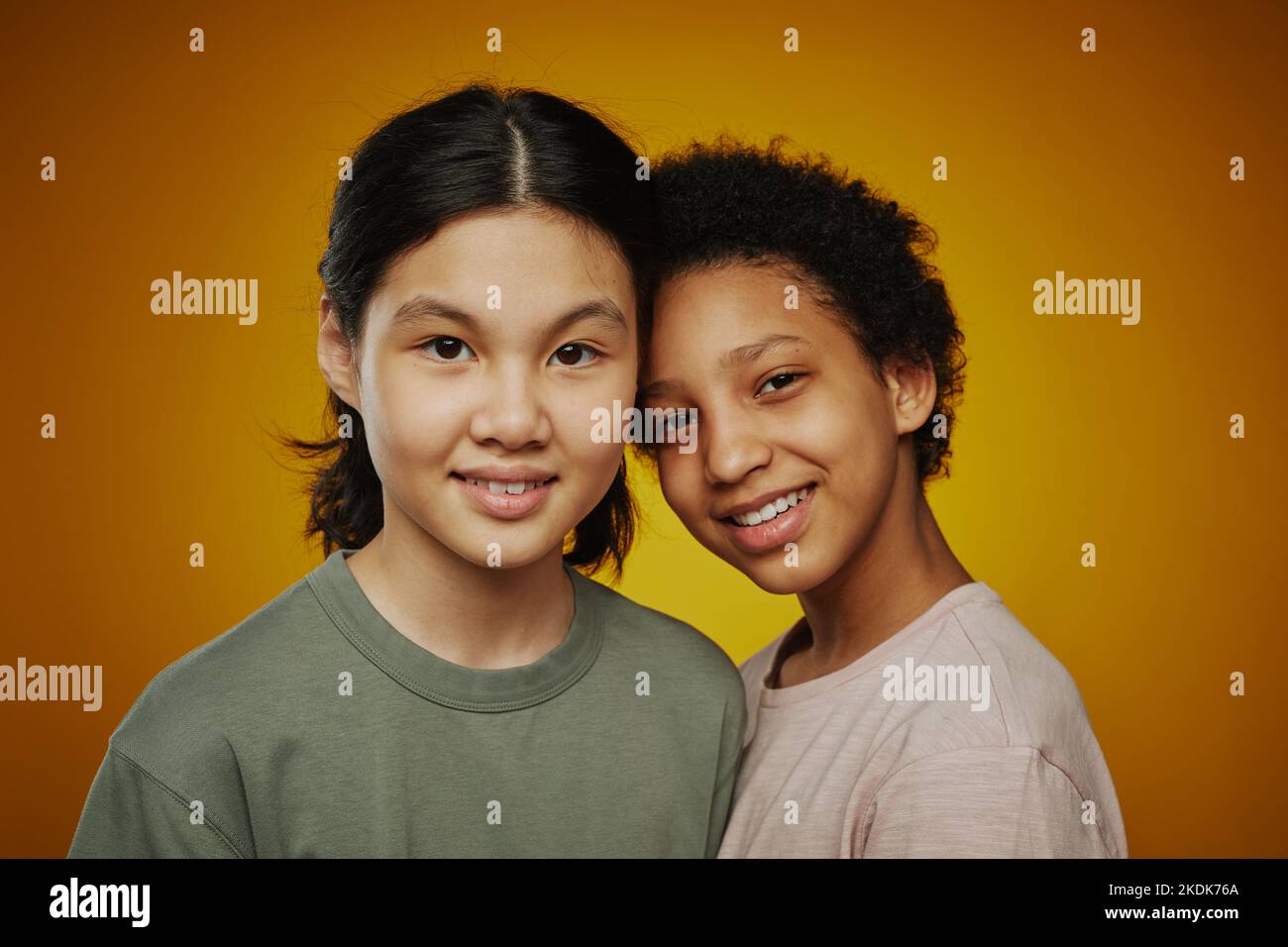 Petit groupe de jolies filles interculturelles pré-adolescentes en t-shirts debout à proximité les uns des autres et regardant la caméra sur fond jaune Banque D'Images