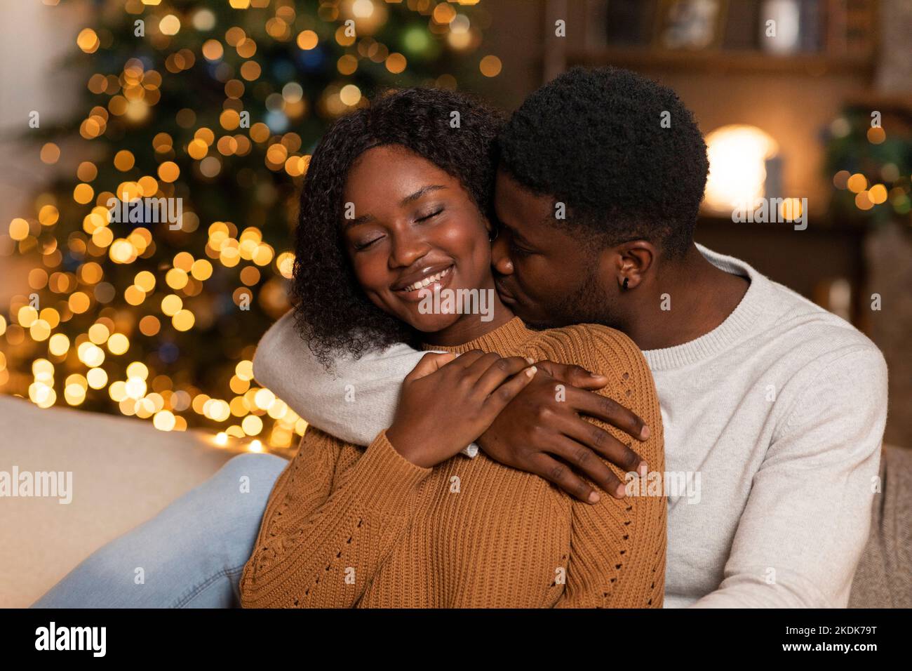 Jeune mari noir souriant câlin et femme baiser, profitez de vacances ensemble dans le salon intérieur avec arbre de Noël Banque D'Images