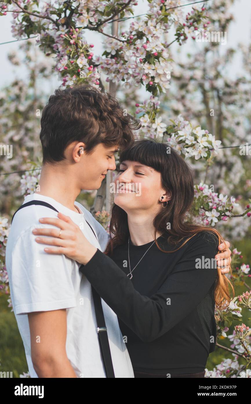 Beau amour fort entre deux jeunes marchant sous des pommiers. Portrait franc d'un couple en vêtements décontractés. Sourire d'un jeune couple. Banque D'Images