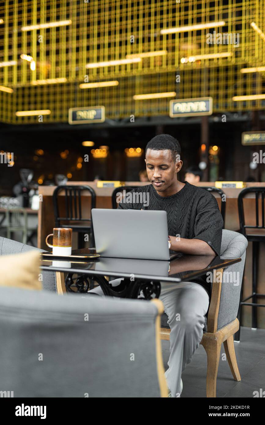 Portrait d'un beau jeune homme noir utilisant un ordinateur portable dans un café Banque D'Images
