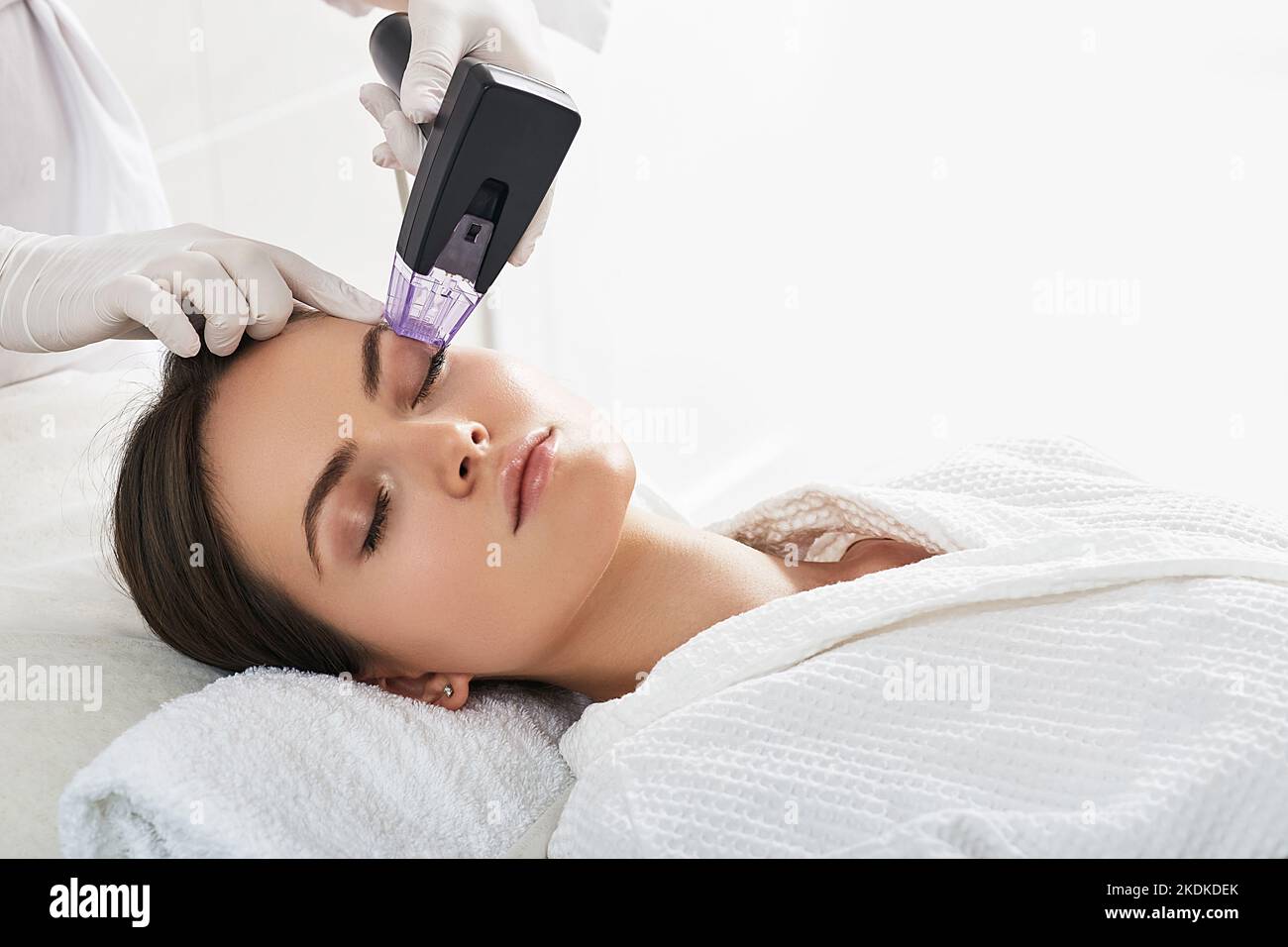 Femme brune aux cheveux recevant une procédure de levage de radiofréquence autour des yeux pour son visage rajeunissement de la peau au centre esthétique de cosmétologie Banque D'Images