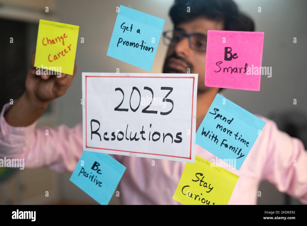 Jeune homme collant 2023 résolutions en utilisant des notes adhésives au bureau - concept de la préparation de la nouvelle année et de l'établissement des objectifs Banque D'Images