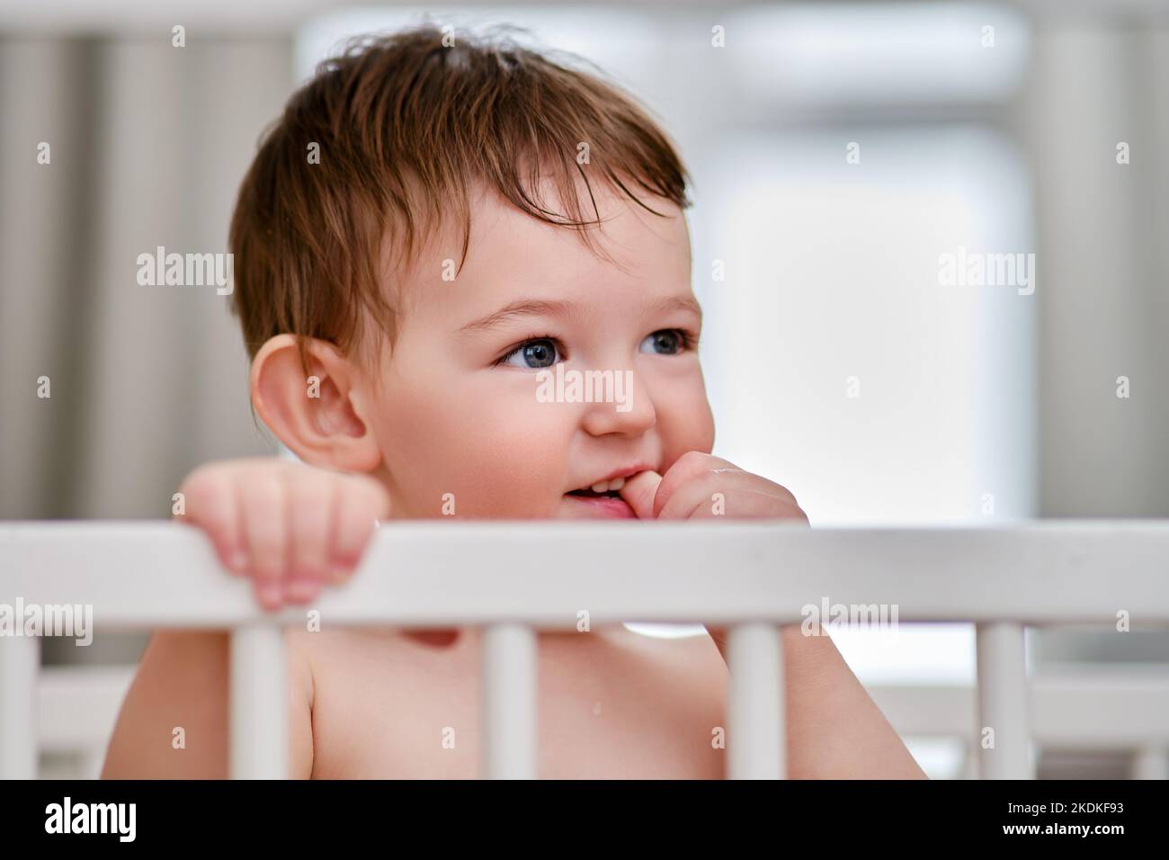 Bébé se tient à penser dans le berceau, portrait en gros plan. L'enfant morce ses ongles sur les doigts, le visage de bébé. Kid est un garçon âgé d'un an et de quatre mois Banque D'Images