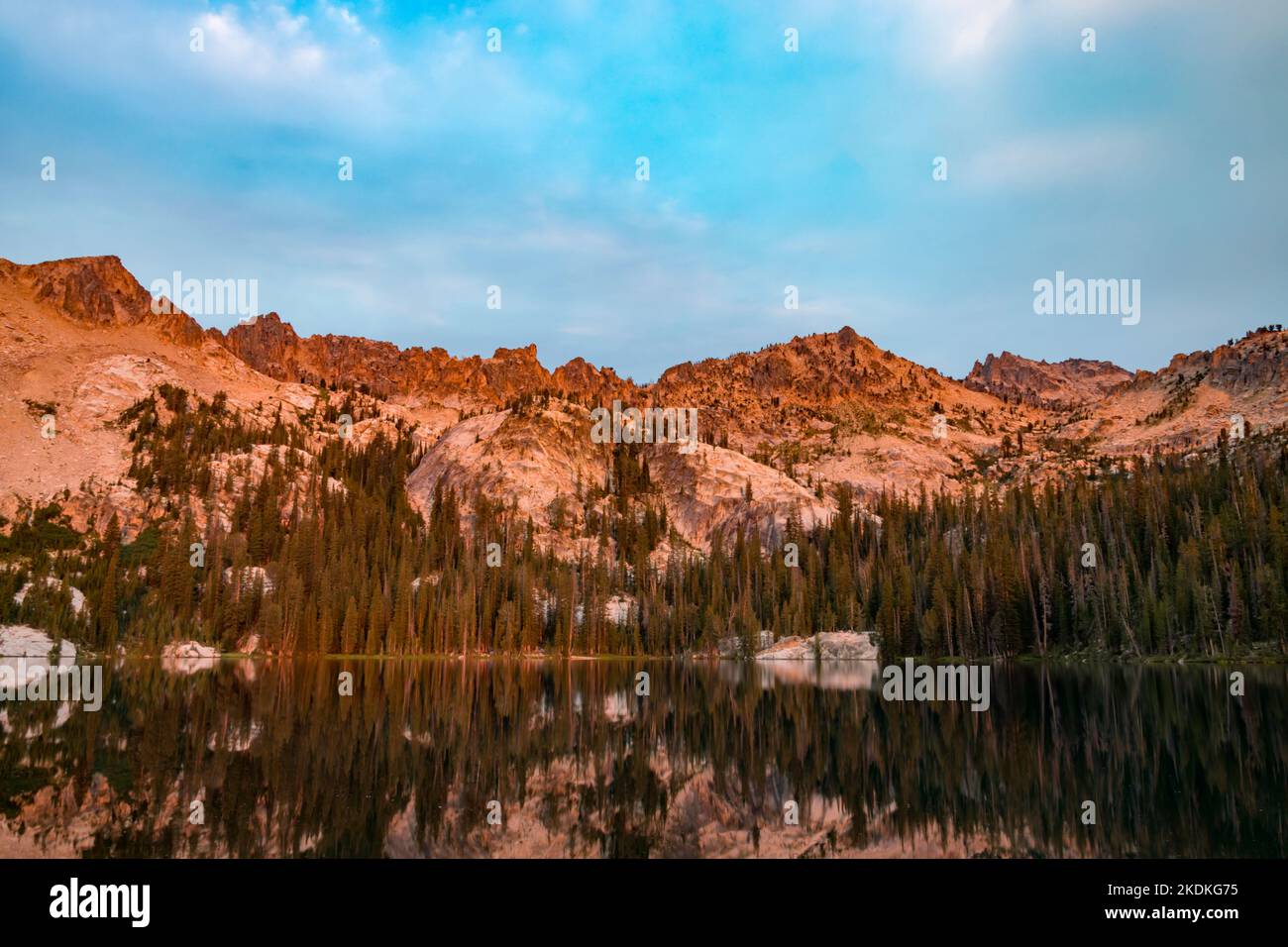 Alpine Lake, situé dans la région sauvage de Sawtooth en Idaho, vu à l'aube un matin d'été, avec lumière du soleil orange illuminant Packrat et Monte Verita Peak Banque D'Images