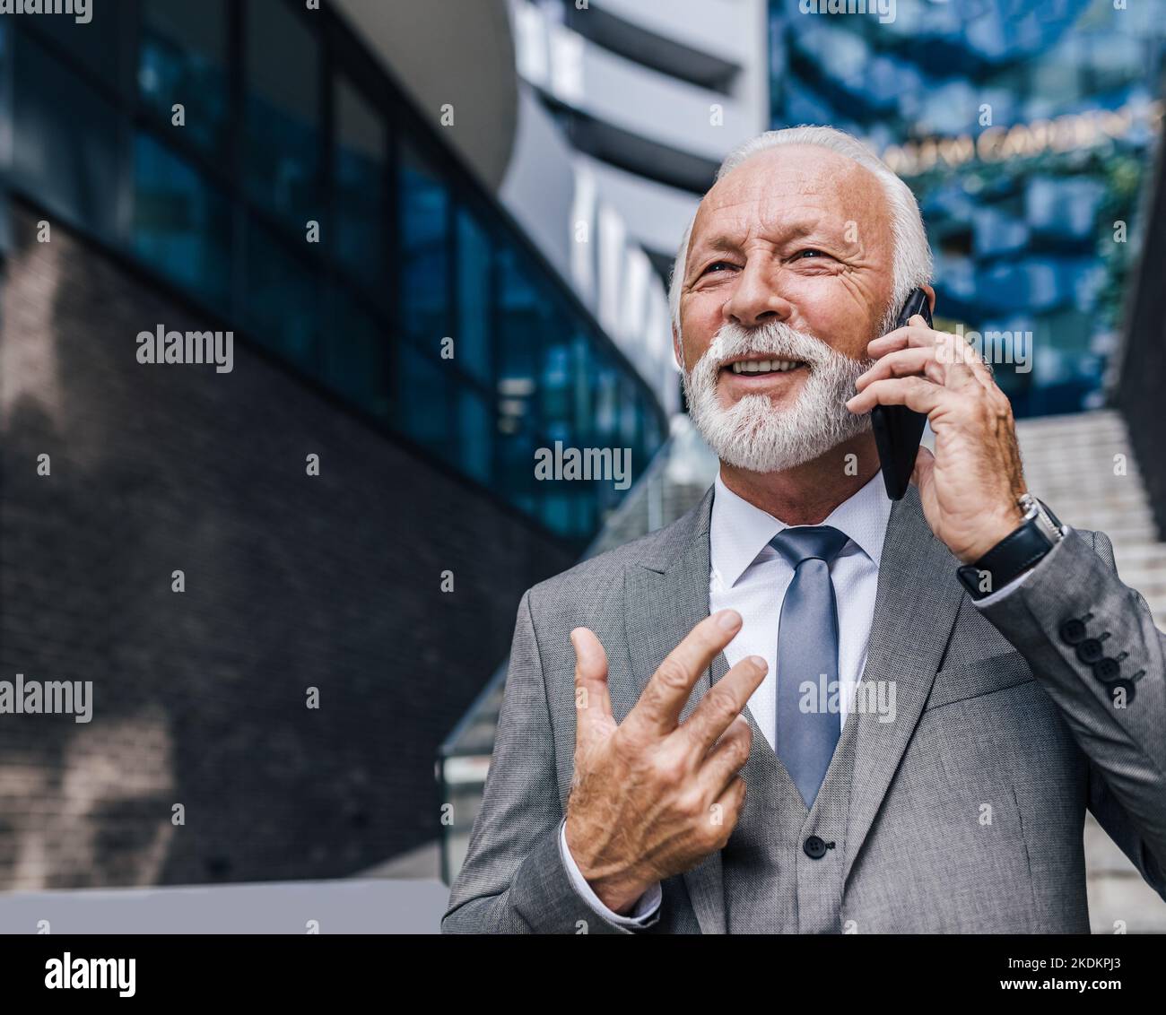 Homme d'affaires souriant parlant au téléphone portable. Homme entrepreneur âgé confiant porte la combinaison complète. Il gestuelle en se tenant contre des offi Banque D'Images