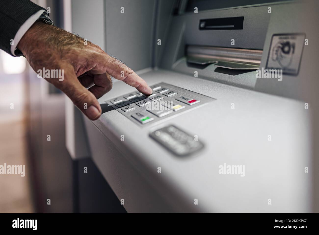 Image rognée d'un homme d'affaires saisissant le code PIN dans un distributeur automatique de billets. Un gros plan d'un professionnel de sexe masculin retire de l'argent. Il utilise la banque électronique. Banque D'Images