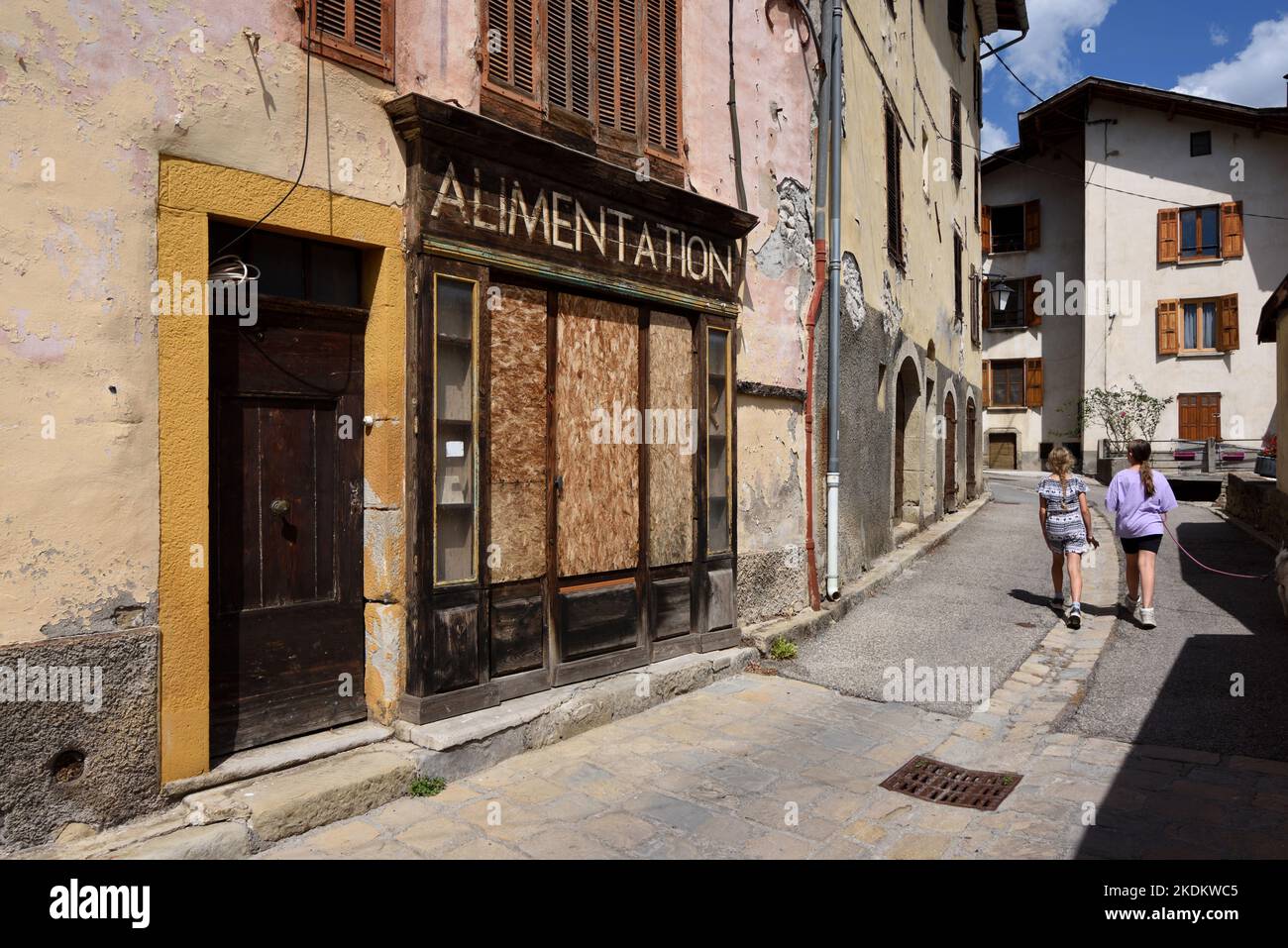 Les jeunes filles marchent devant une boutique de village vacante, fermée, arraisonnée ou abandonnée ou une boutique d'angle à Beauvezer Alpes-de-haute-Provence Provence Provence France Banque D'Images