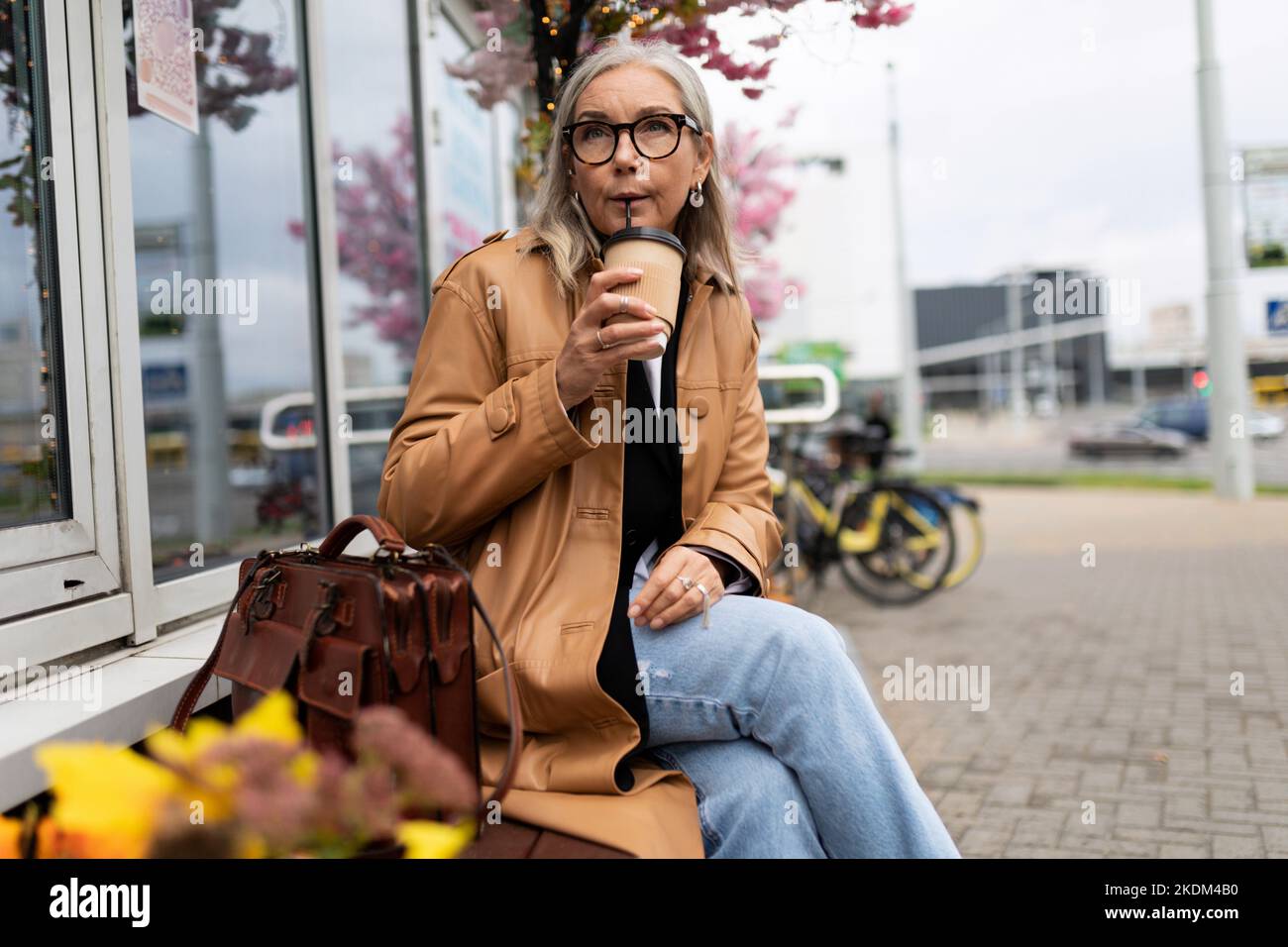 femme âgée buvant du café sur un banc près du magasin Banque D'Images