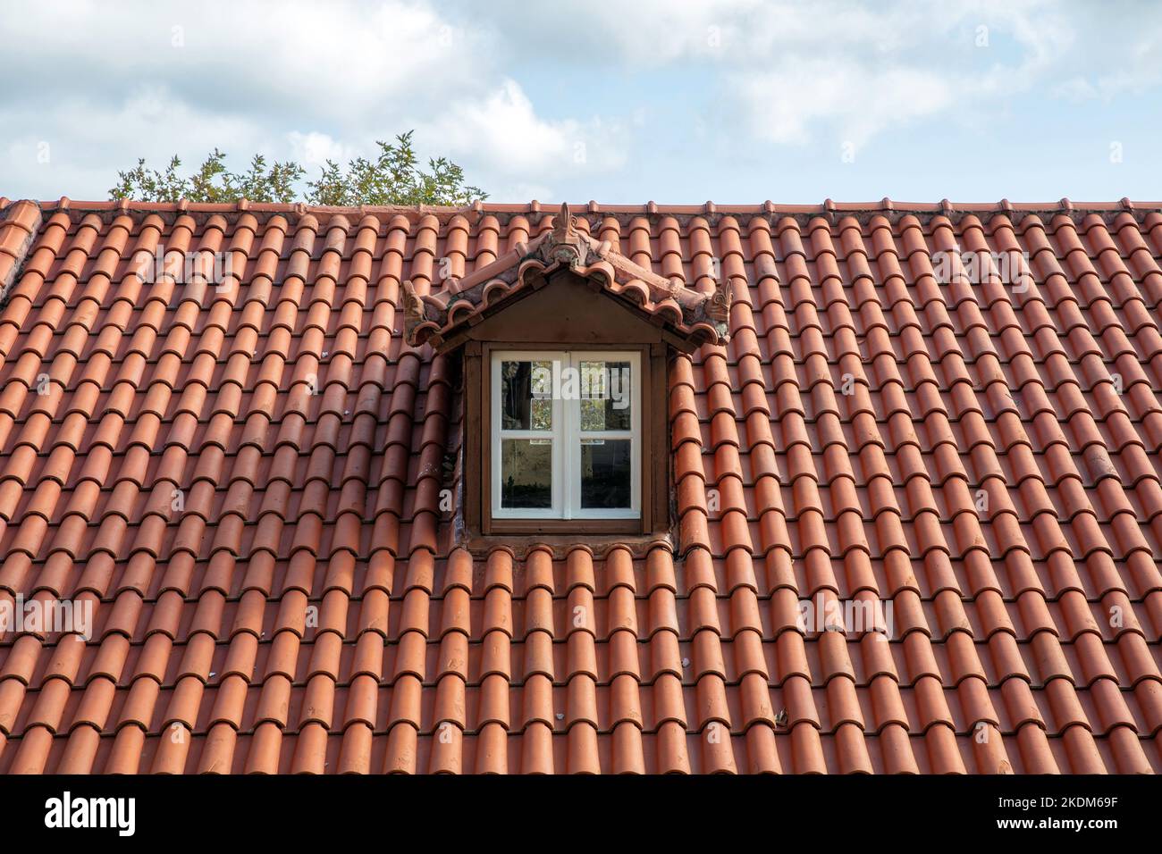 Toit carrelé rouge avec grenier. Fenêtre Dormer de couleur blanche sur la garret, sur le toit. Fond ciel nuageux. Banque D'Images