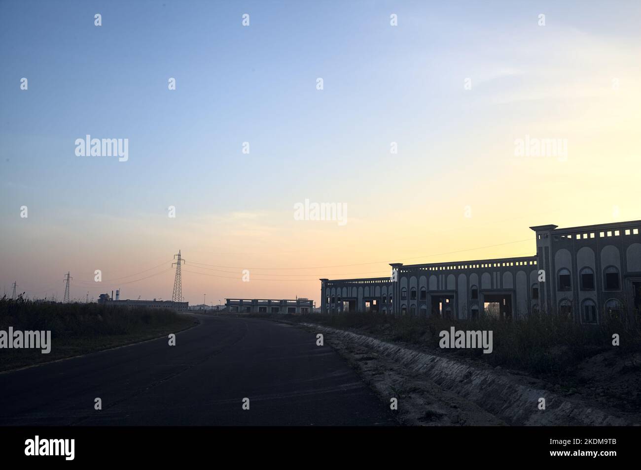 Route vide avec des entrepôts et des pylônes abandonnés au coucher du soleil Banque D'Images