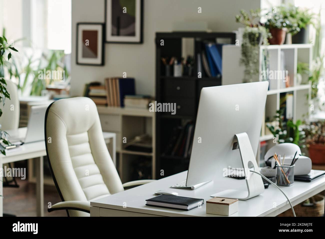 Moniteur d'ordinateur debout sur le lieu de travail de l'employé de bureau avec ordinateur portable et autres fournitures et fauteuil en cuir blanc à proximité Banque D'Images