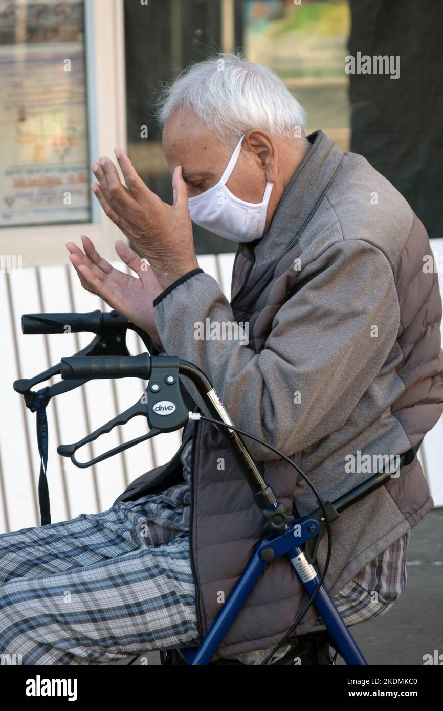 Un homme musulman plus âgé prie sur Diversity Plaza tout en étant assis sur son marcheur. À Jackson Heights, Queens, New York. Banque D'Images