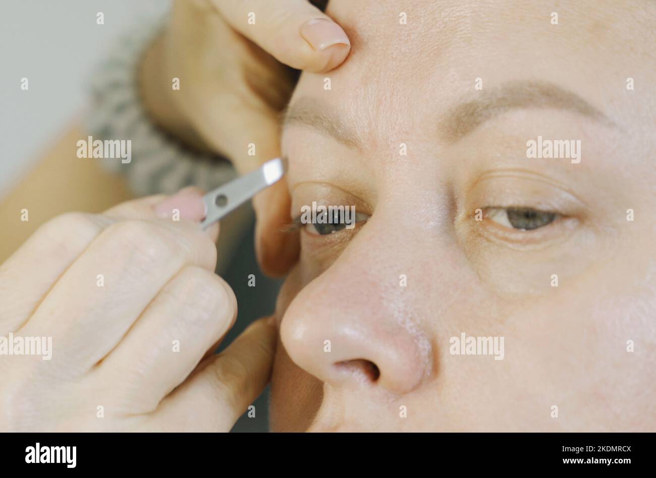 Les mains du styliste plisent les sourcils avec une pince à épiler sur le visage d'une femme. Gros plan. Soins du visage. Banque D'Images