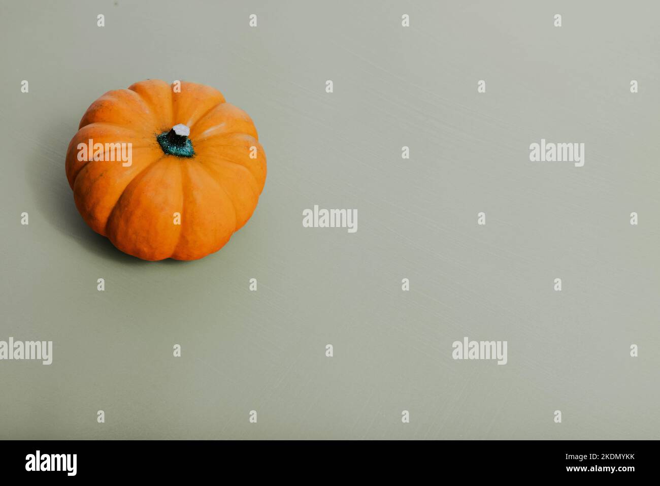 Une seule citrouille orange miature sur fond vert clair beige Banque D'Images