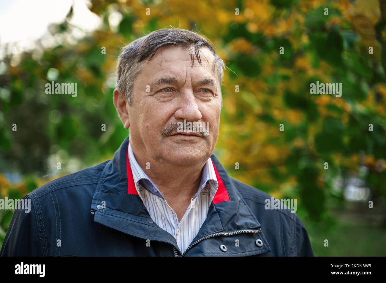 un homme âgé de 70 ans se repose sur un banc à l'automne. L'homme sourit en regardant la caméra. Optimisme et confiance dans l'âge adulte. Banque D'Images