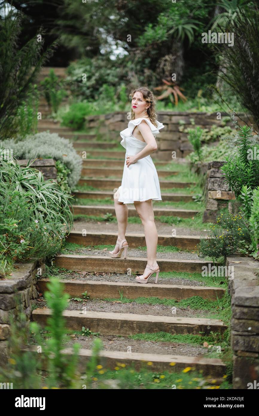 Femme portant une robe blanche courte debout sur un chemin de jardin Banque D'Images