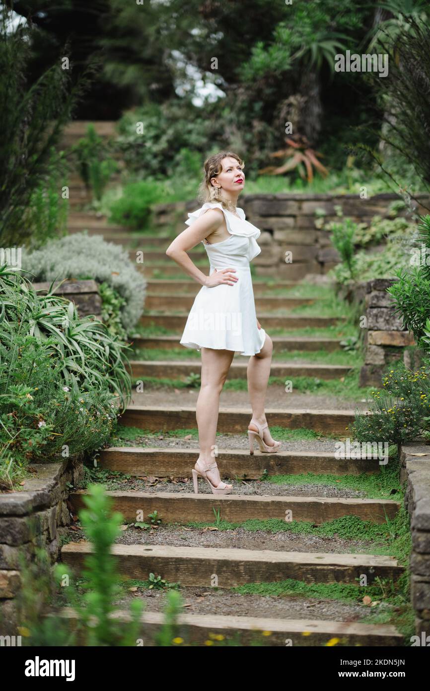 Femme portant une robe blanche courte debout sur un chemin de jardin Banque D'Images