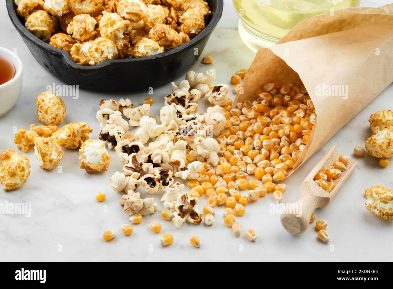 Pop-corn préparé dans une poêle, grains de maïs séchés, sauce caramel et bouteille d'huile sur une table de cuisine. Banque D'Images