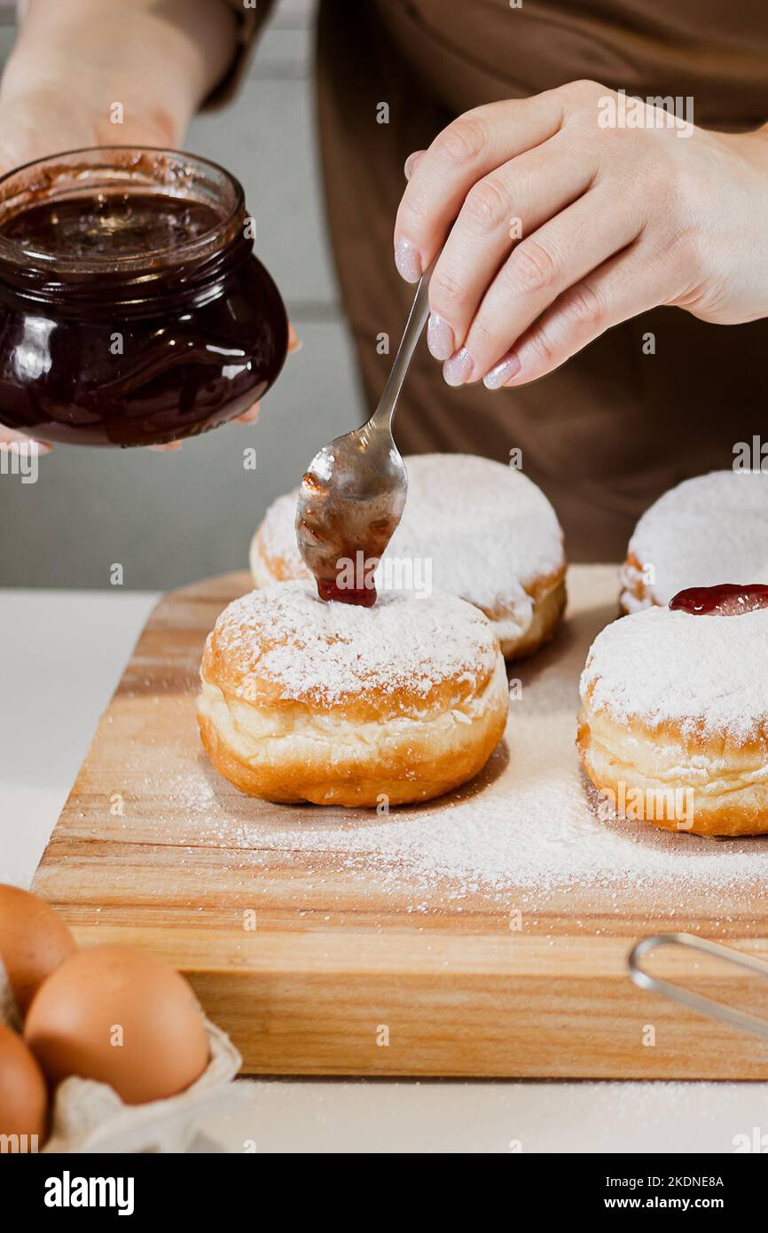 Cuisine traditionnelle Hanukkah sufganiyot.Une femme décore des beignets avec de la confiture.Dessert juif festif. Banque D'Images