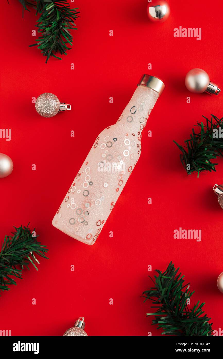 Nouveau concept de l'année en bouteille, branches de sapin et boules de Noël sur fond rouge. Idée de fête minimale. Flat lay, vue de dessus. Banque D'Images