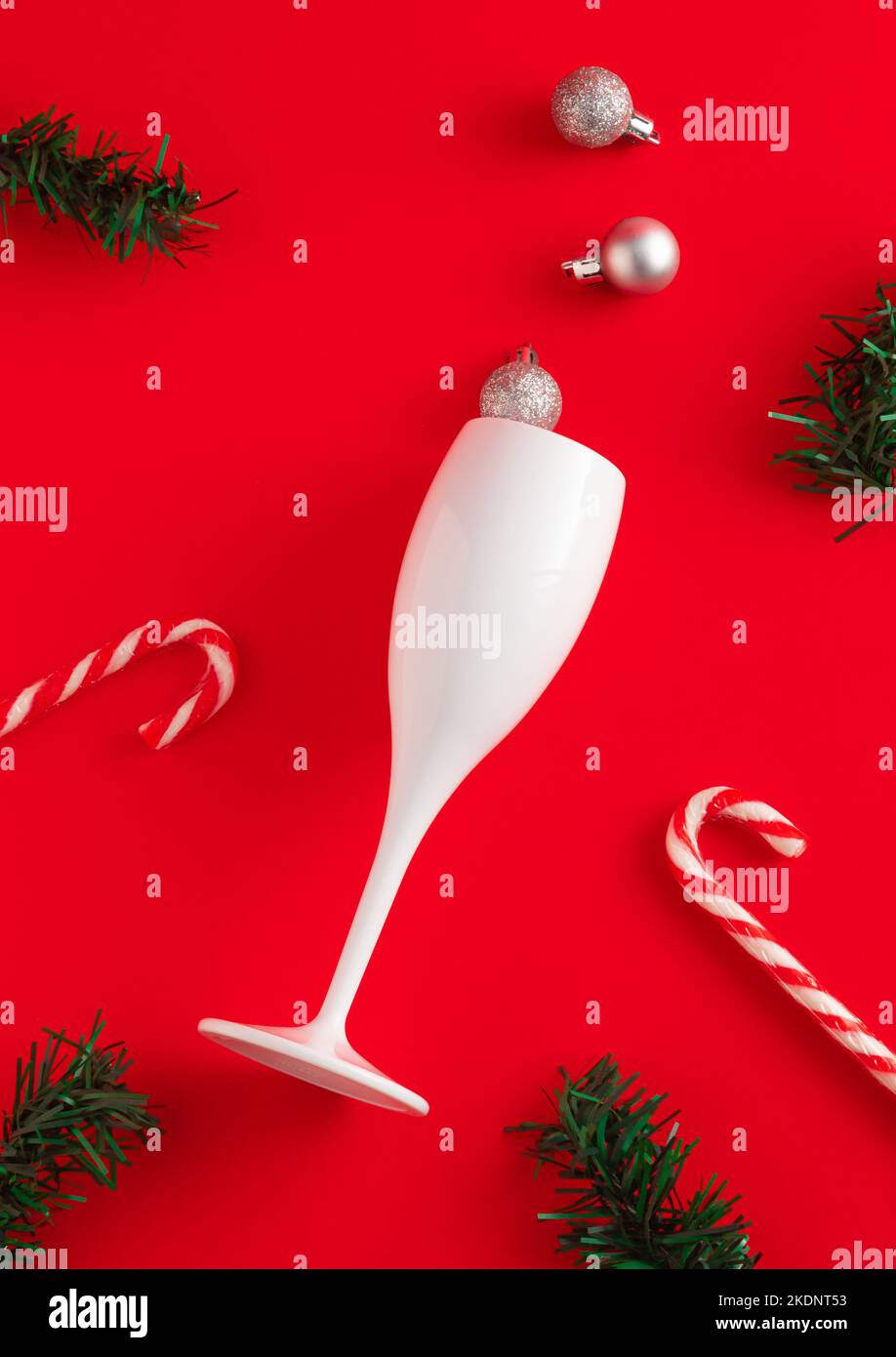 Nouveau concept de l'année en verre à vin, bonbons, branches de sapin et boules de Noël sur fond rouge. Idée de fête minimale. Flat lay, vue de dessus. Banque D'Images