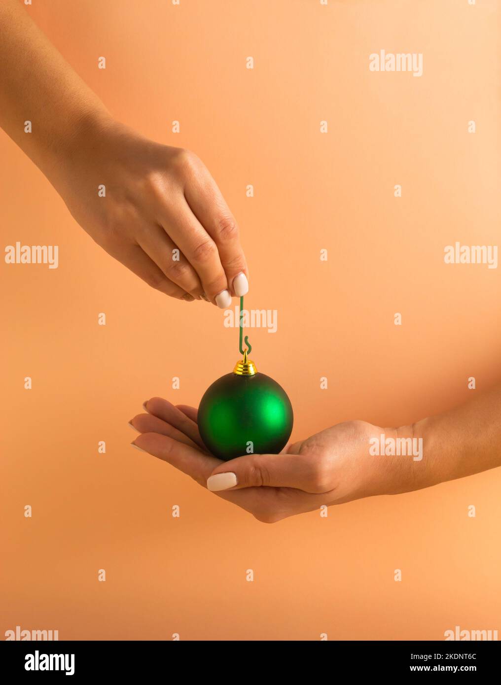 Mains de femme tenant une boule de Noël verte sur fond orange pastel. Concept de vacances minimal. Bonne Année. Banque D'Images