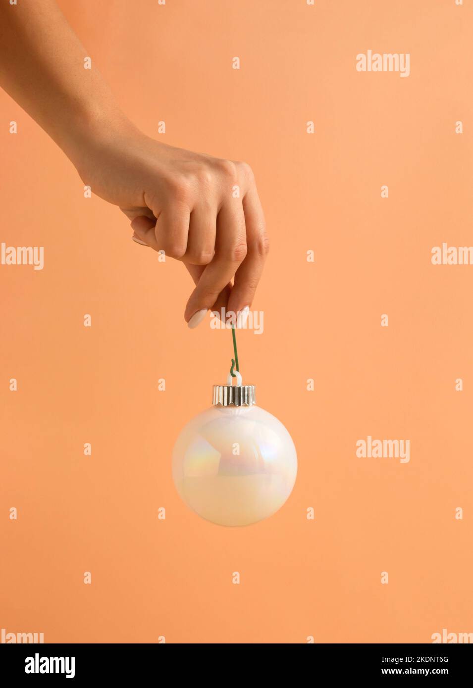 Composition de Noël minimaliste faite de la main de femme tenant blanc brillant boule de Noël sur fond orange pastel. Bonne Année. Banque D'Images