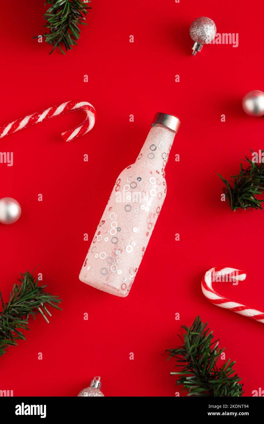 Nouveau concept de l'année en bouteille, bonbons, branches de sapin et boules de Noël sur fond rouge. Idée de fête minimale. Flat lay, vue de dessus. Banque D'Images