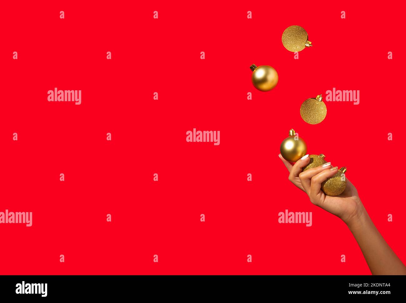 La main de femme jonglant avec des boules de Noël dorées sur fond rouge. Concept de vacances minimal. Bonne Année. Copier l'espace. Banque D'Images