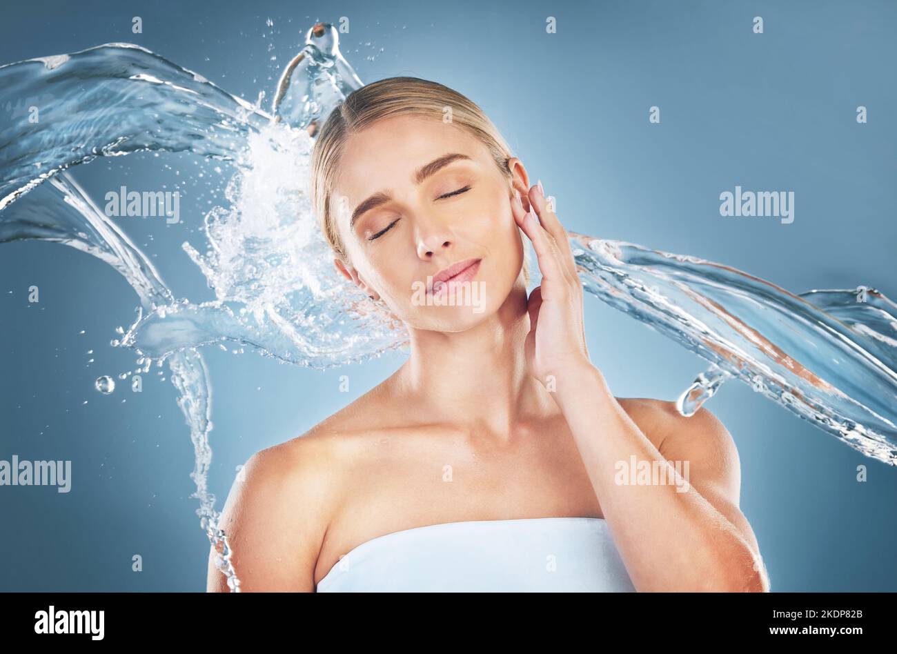 Visage, beauté et éclaboussures d'eau de la femme avec les yeux fermés  isolés sur un fond bleu en studio. Hygiène du soin de la peau, nettoyage du  visage et jeunes femmes Photo