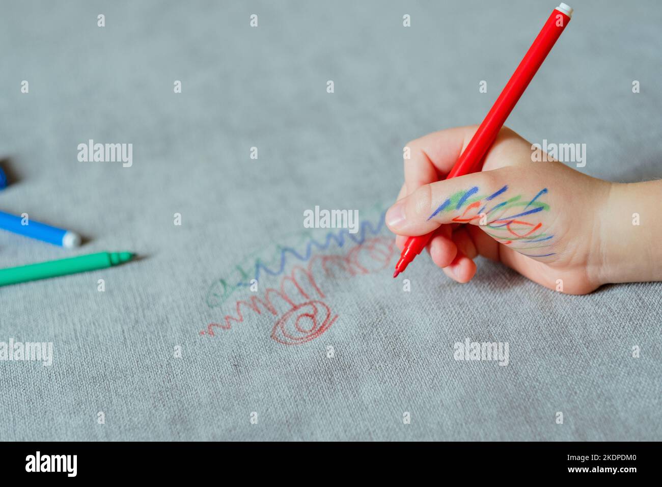 Un enfant est taché d'encre à la main, en dessinant avec un marqueur rouge sur la sellerie du canapé. Tissus de mobilier. Concept de nettoyage Banque D'Images