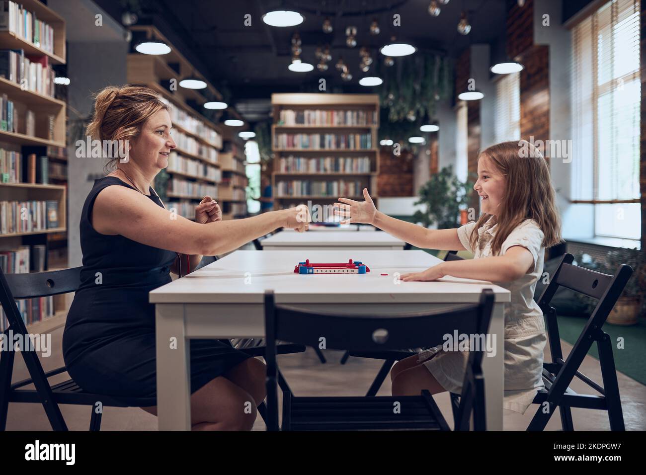 Professeur jouant avec une écolière rock, papier, jeu de ciseaux dans le club de l'après-école. Enfant jouant avec un professeur dans la bibliothèque de l'école après les cours au primaire Banque D'Images