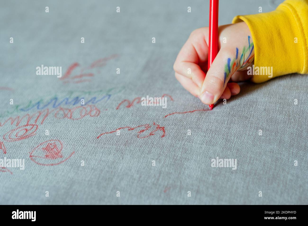 Un enfant à main levée dessine un stylo feutre rouge sur la sellerie du canapé. Tissus de mobilier. Concept de nettoyage Banque D'Images