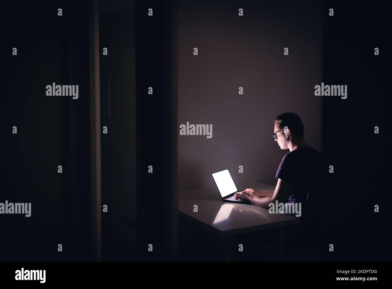 Travail de nuit avec ordinateur portable dans une salle de bureau sombre. Jeune homme utilisant un ordinateur portable. Codeur, programmeur, hacker, éditeur numérique indépendant ou étudiant. Banque D'Images