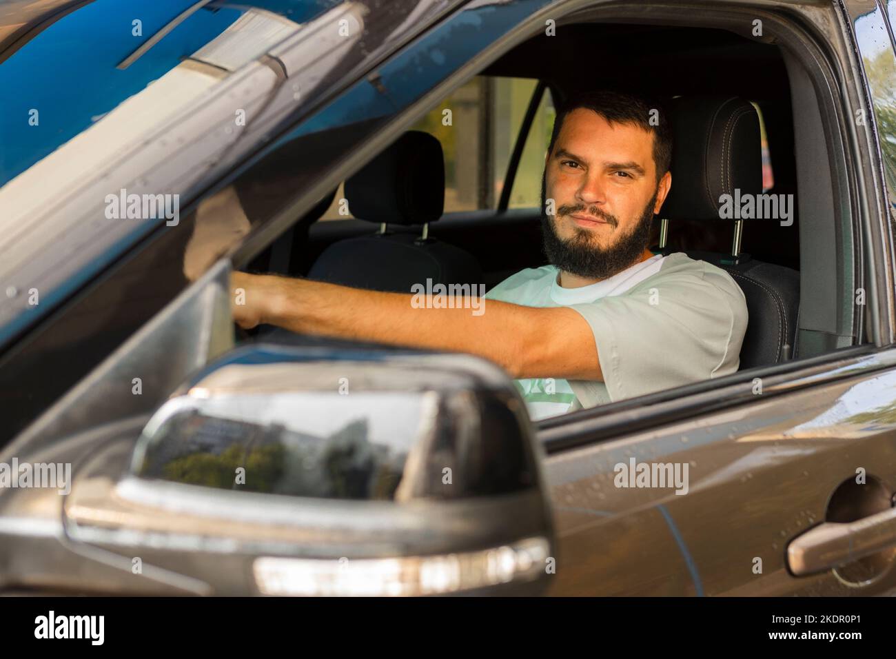 Jeune conducteur heureux derrière le volant à l'intérieur de la nouvelle voiture. Scène de style de vie dans la concession automobile Banque D'Images