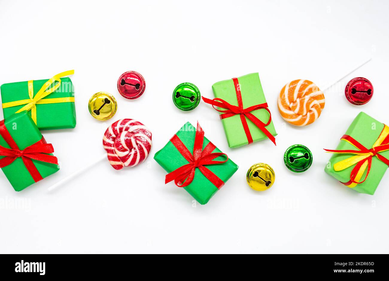 Joyeuses fêtes: Cadeaux avec des sucettes et des cloches rouges, vertes, dorées sur fond blanc, espace copie. Le concept de Noël, ventes, fêtes pour enfants Banque D'Images