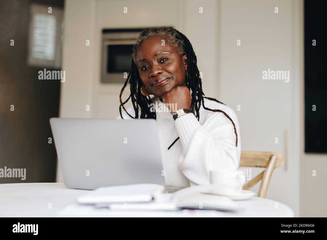 Femme d'affaires senior regardant la caméra tout en travaillant sur un ordinateur portable à la maison. Femme d'affaires mature qui fait du travail indépendant en ligne dans son bureau à domicile. Banque D'Images