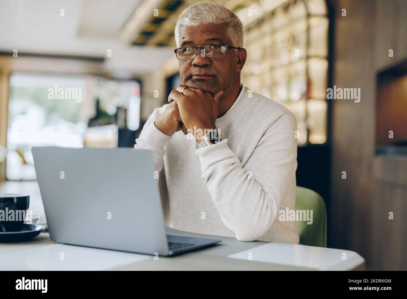 Homme d'affaires mature regardant la caméra tout en travaillant dans un café moderne. Homme d'affaires senior utilisant un ordinateur portable tout en travaillant à distance. Banque D'Images