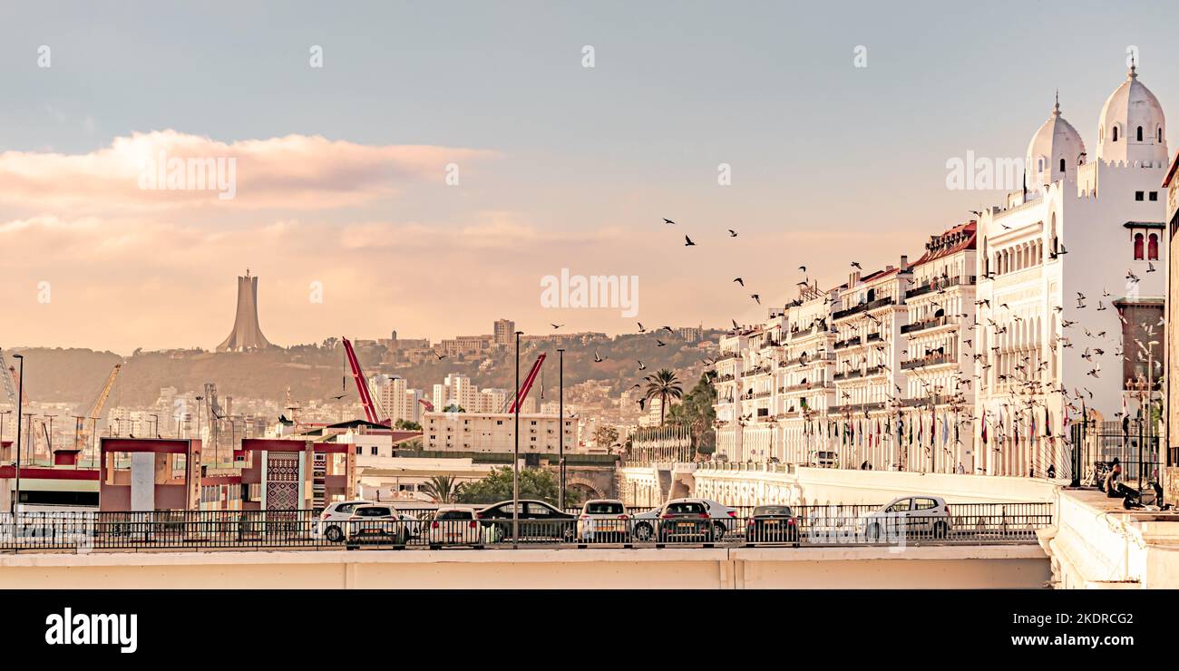 Bâtiment du siège de wilaya avec vol d'oiseaux, voitures garées et drapeaux arabes. Le monument commémoratif du Martyr et un ciel bleu coudy. Banque D'Images