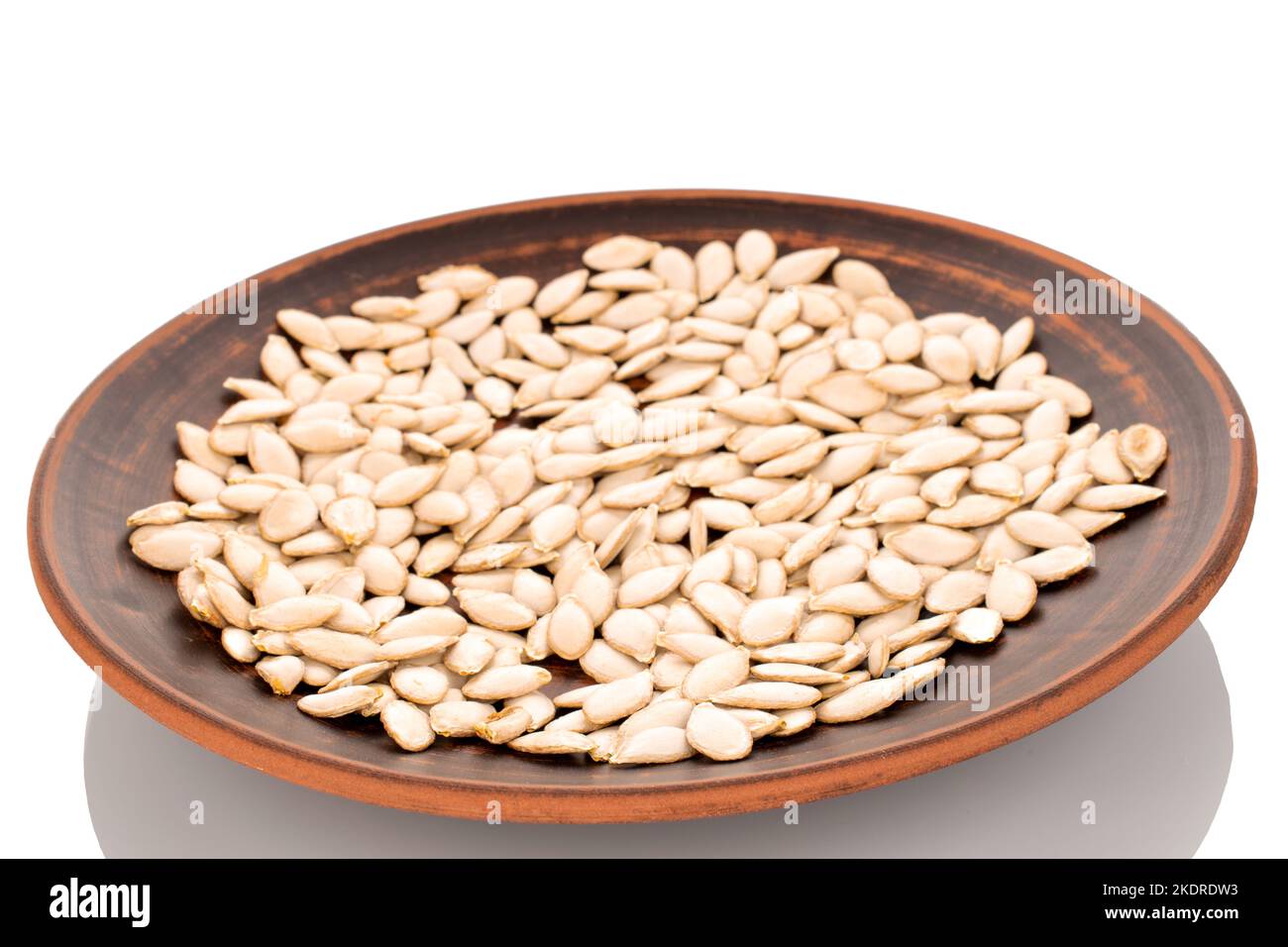 Graines de citrouille brutes non pelées dans une plaque d'argile, macro, isolée sur fond blanc. Banque D'Images