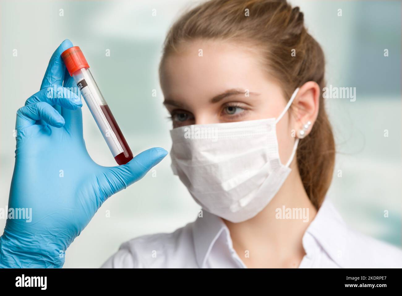 une jeune femme avec un masque médical et des gants médicaux manipule un tube à sang dans un laboratoire Banque D'Images