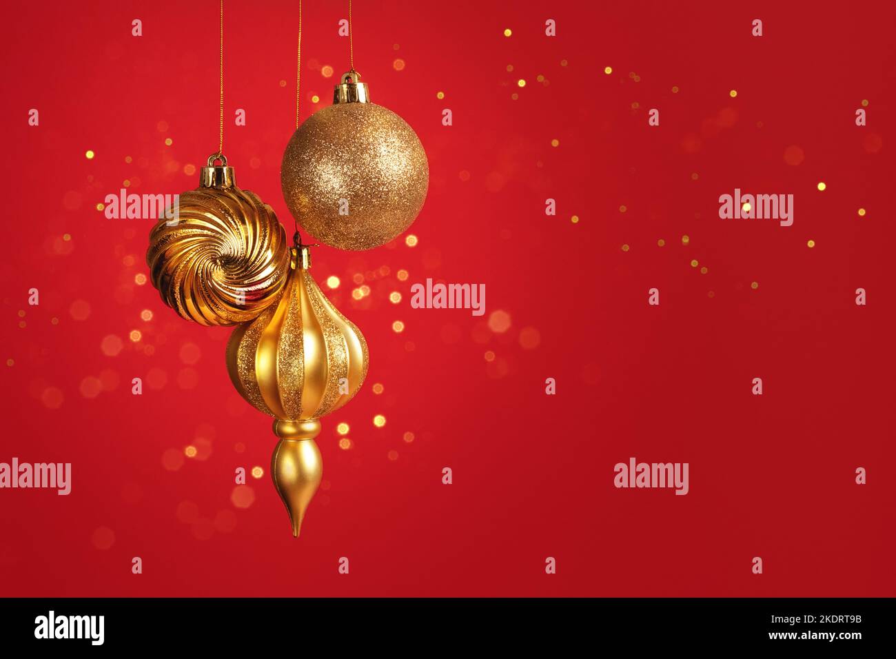 Carte de Noël avec trois boules dorées sur fond rouge et lumières bokeh Banque D'Images