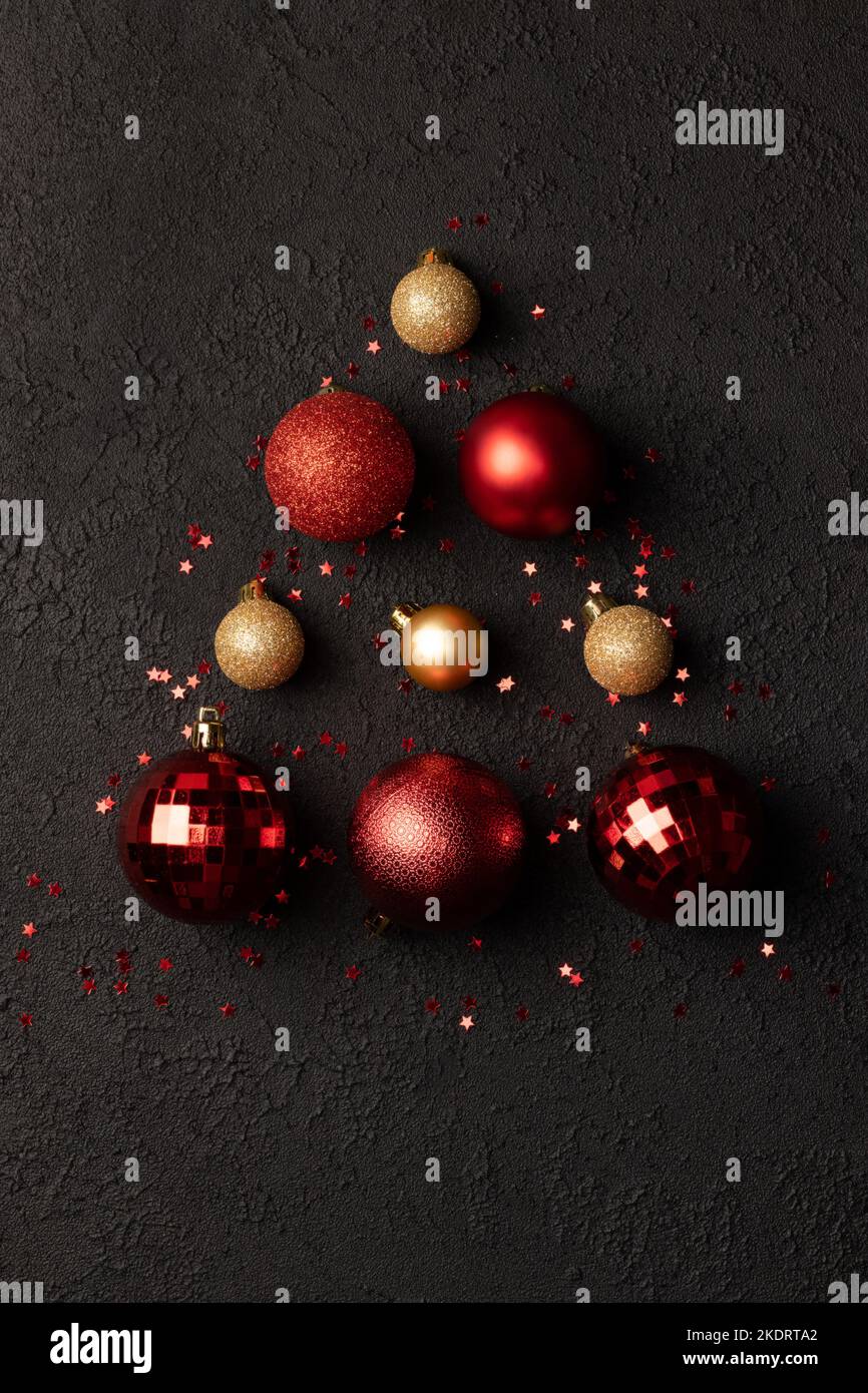 Sapin de Noël en boules décoratives rouges et dorées, et étoiles confettis à paillettes sur fond noir Banque D'Images