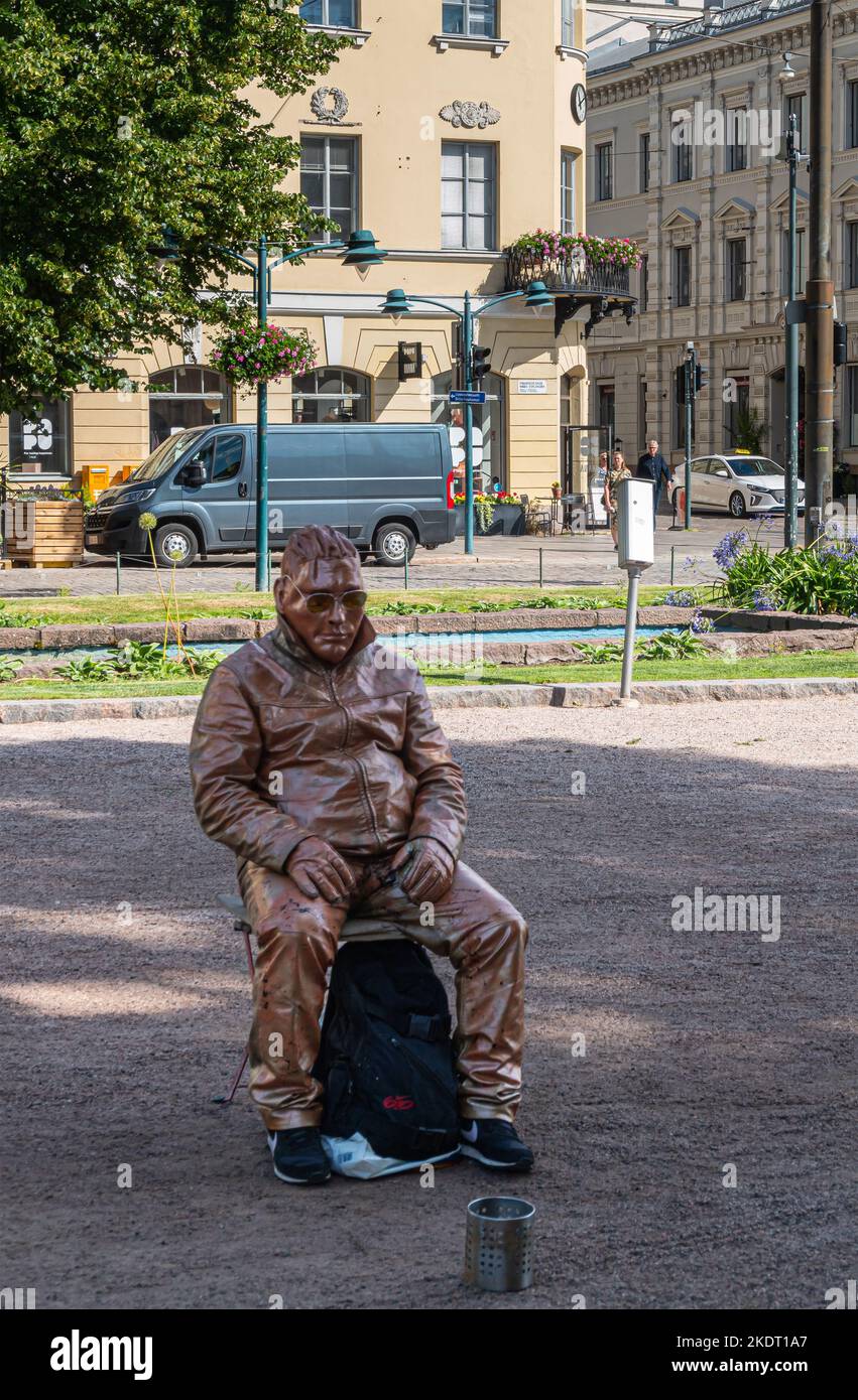 Helsinki, Finlande - 19 juillet 2022 : gros plan d'un homme vivant peint en marron qui se pose comme une statue gelée dans le parc tout en implorant de l'argent. Façades vertes de son Banque D'Images