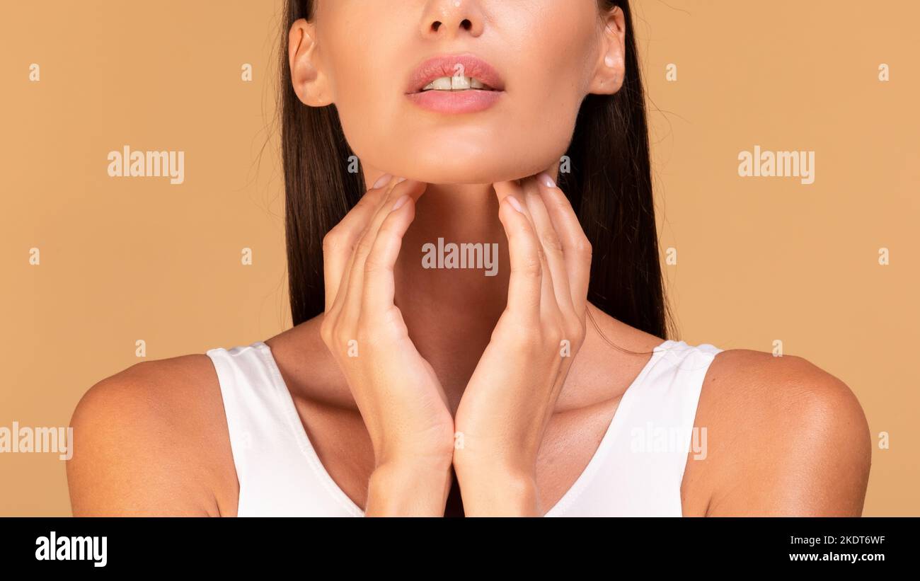 Gros plan d'une jeune femme souffrant de douleurs dans la gorge, touchant son cou, panorama, arrière-plan beige studio Banque D'Images