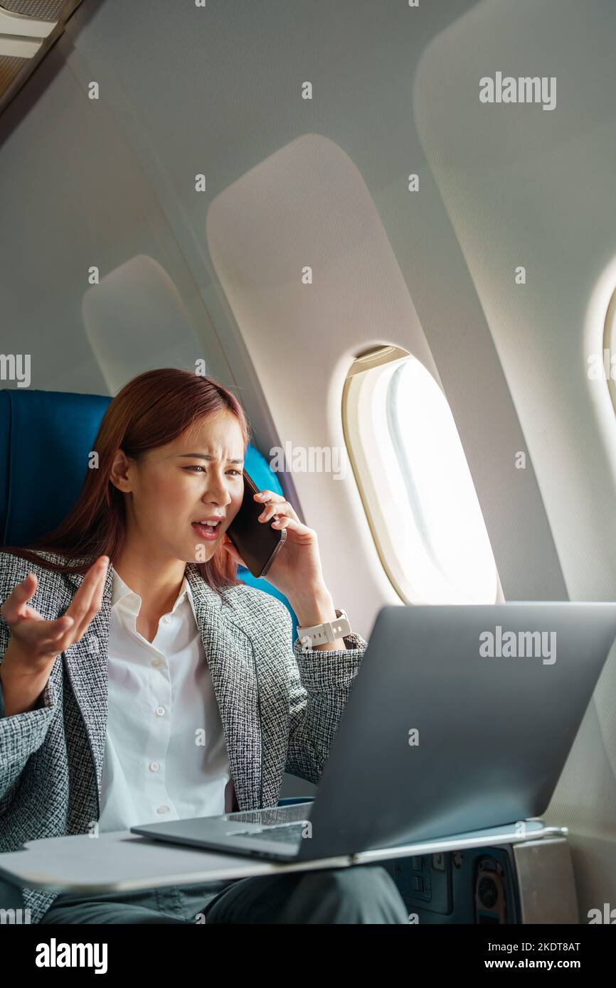 Portrait d'une femme d'affaires ou d'un entrepreneur asiatique couronné de succès dans un costume formel sur un avion assis en classe affaires à l'aide d'un téléphone, ordinateur portable Banque D'Images